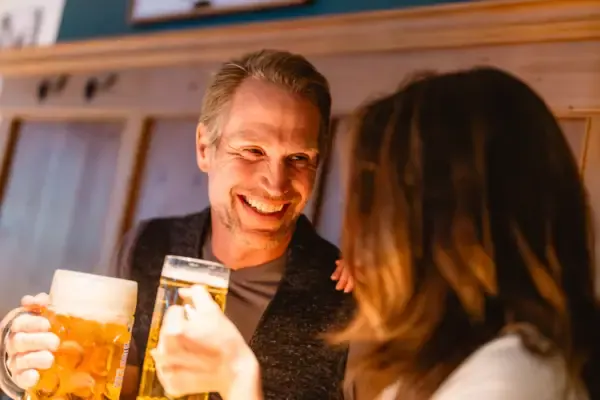 Paar stößt mit Biergläsern in gemütlicher Wirtshausatmosphäre an